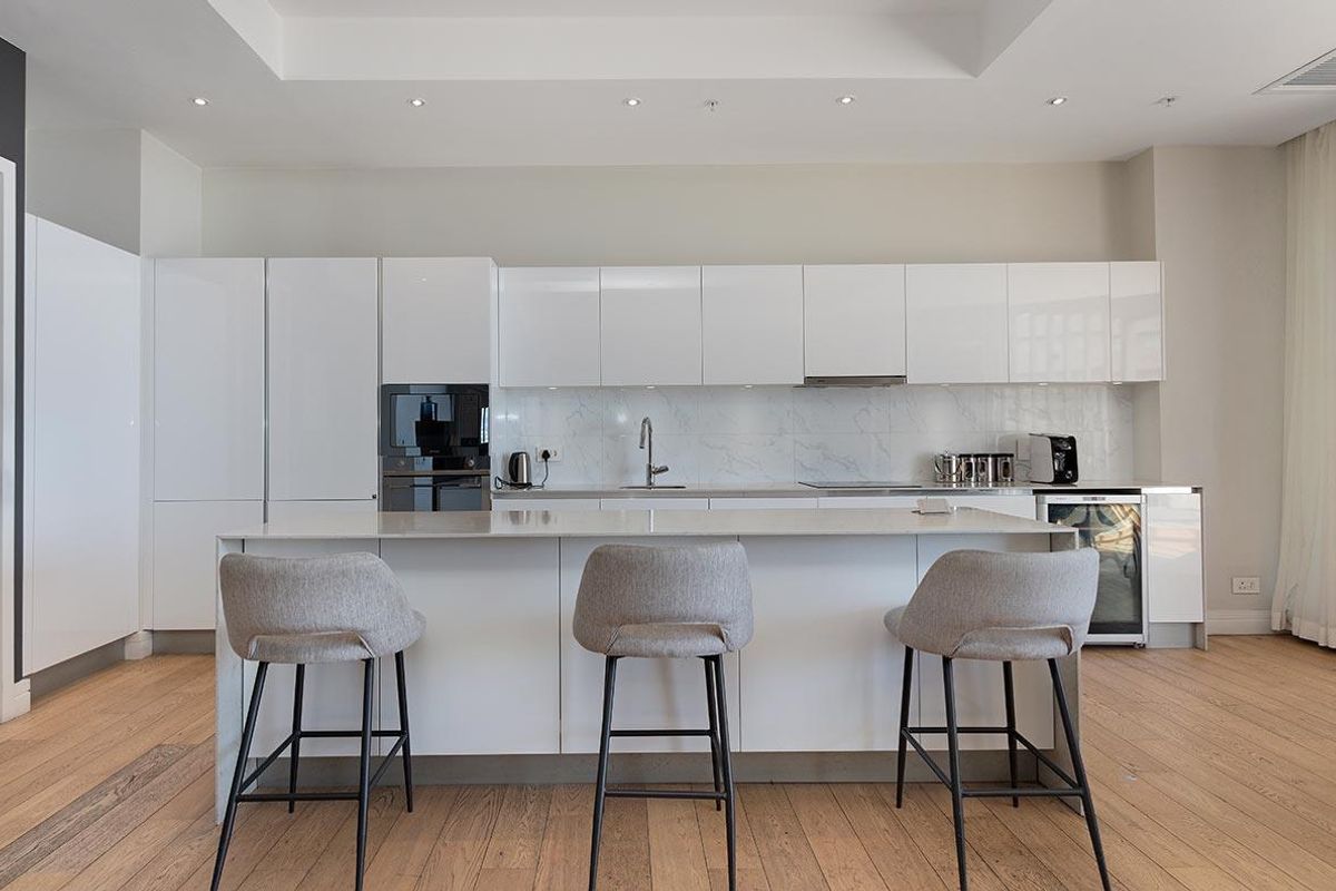 Modern kitchen featuring sleek white cabinetry, stone countertops, integrated appliances, and a central island with breakfast bar seating.