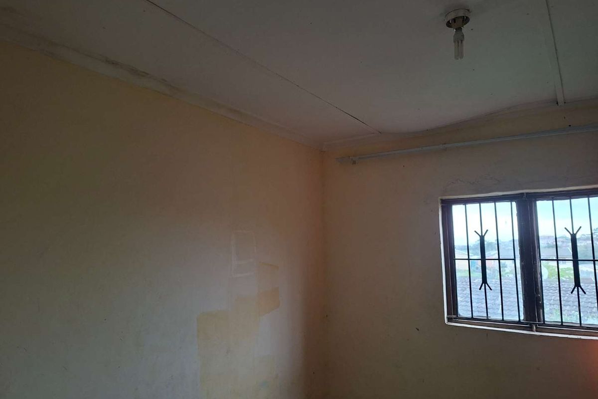 An empty bedroom featuring a window with security bars, requiring cosmetic updates to the walls and ceiling finishes.