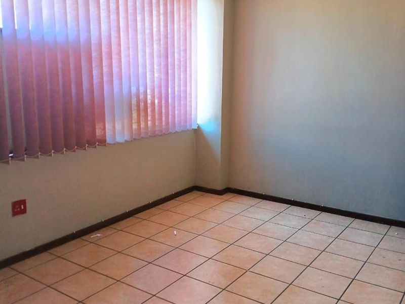 An empty office space featuring neutral walls, tiled flooring, and vertical window blinds, providing a clean and functional environment for professional use.