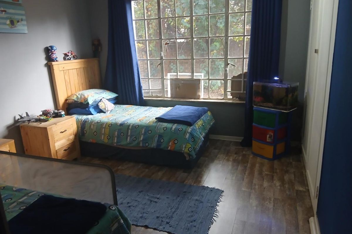 A bedroom featuring wood-look laminate flooring, a large multi-pane window with natural light, and built-in cupboard storage.