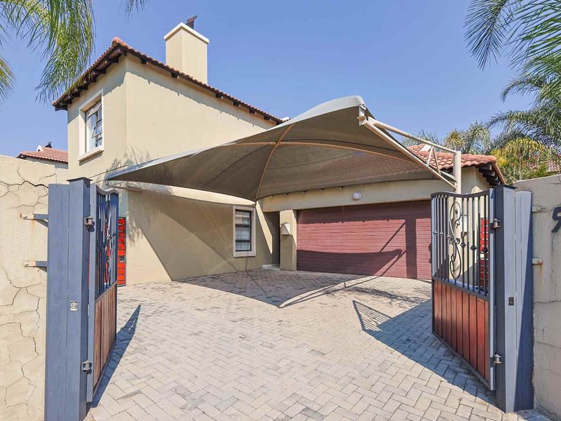 Front exterior view of the property featuring a paved driveway, a shade sail carport, a garage, and a secure gated entrance.