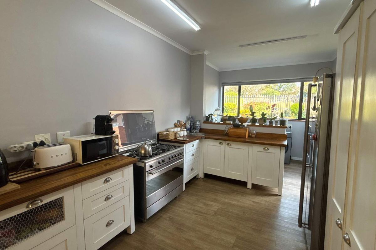A functional kitchen featuring white shaker-style cabinetry, warm wooden countertops, a gas stove, and durable laminate flooring with natural light.