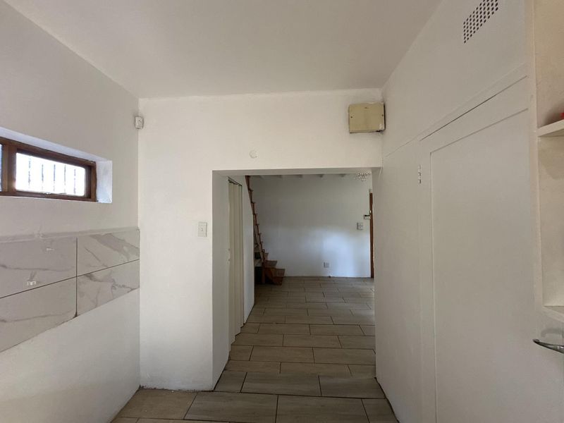 A vacant hallway featuring tiled flooring, built-in storage, and a wooden staircase leading to an upper level.