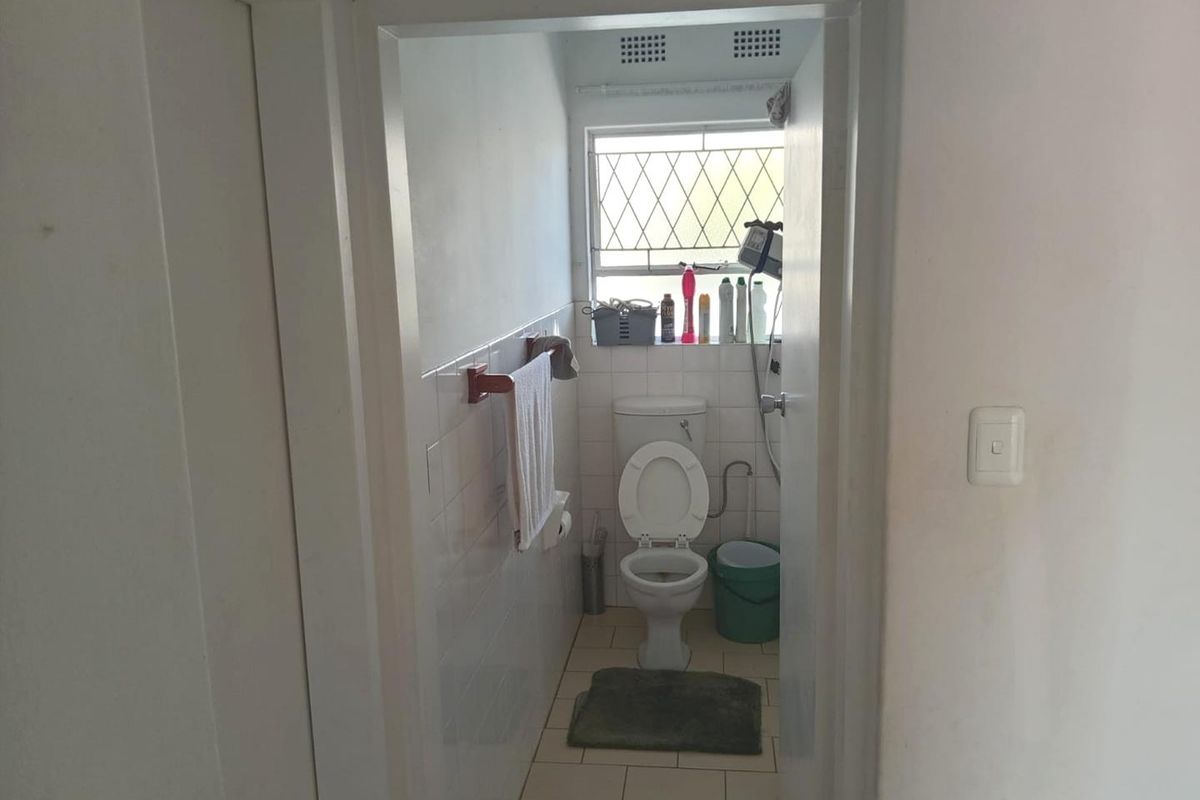 A compact, functional bathroom featuring tiled walls and flooring, a standard toilet, and a window with security bars.
