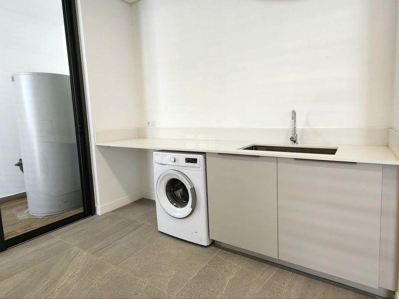 A functional laundry area featuring modern cabinetry, a stone countertop, a stainless steel sink, and tiled flooring.