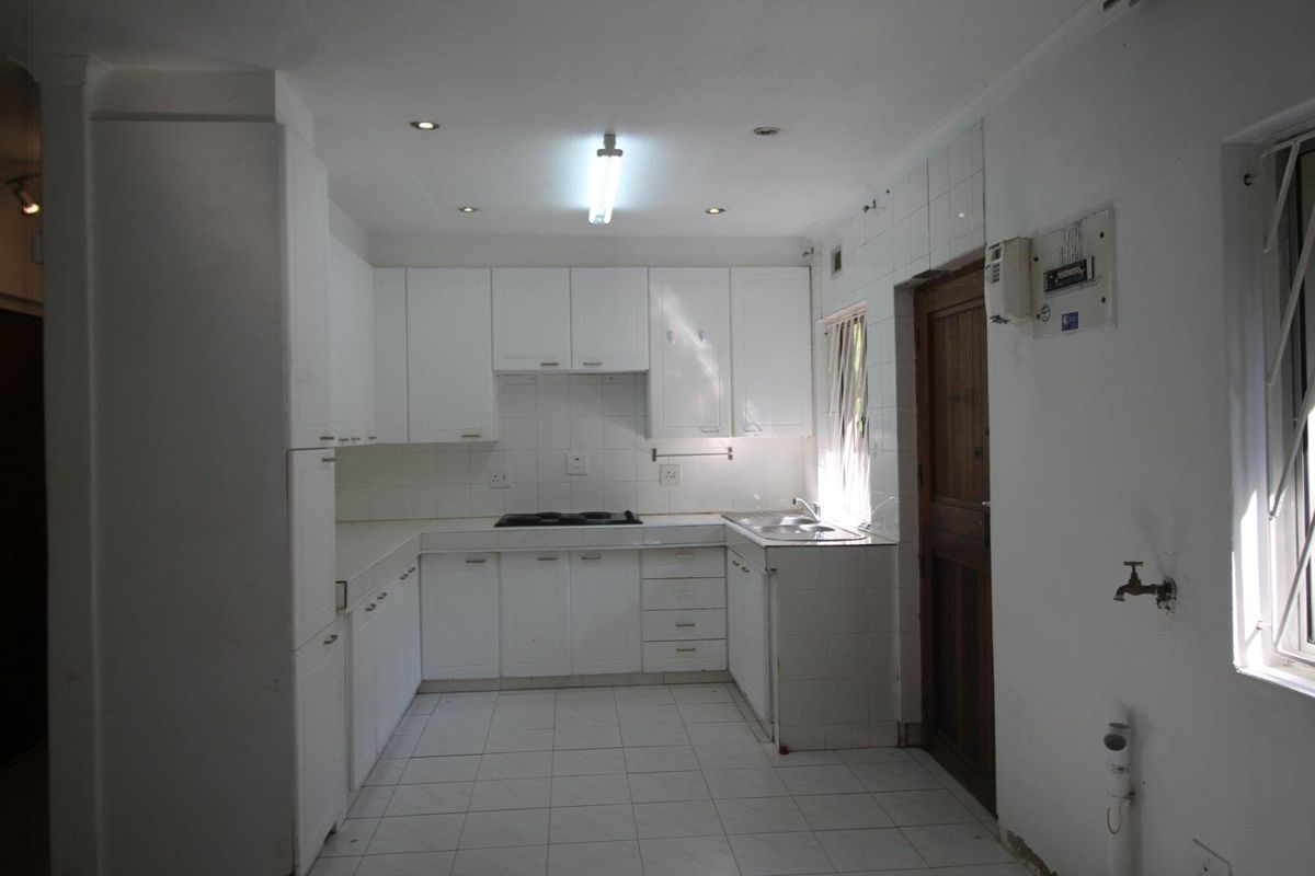 A functional kitchen featuring white cabinetry, tiled countertops, a built-in hob, and a double sink, with direct access to an adjacent room.