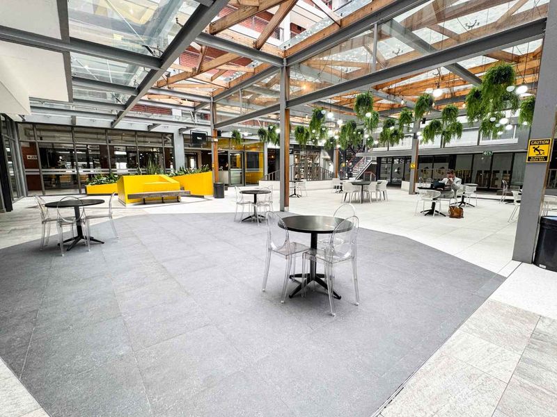 A modern, covered outdoor courtyard featuring a glass roof, steel structural elements, and tiled flooring, suitable for retail or commercial use.
