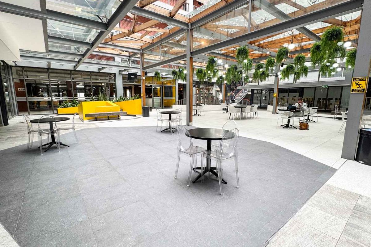A modern, covered outdoor courtyard featuring a glass roof, steel structural elements, and tiled flooring, suitable for retail or commercial use.