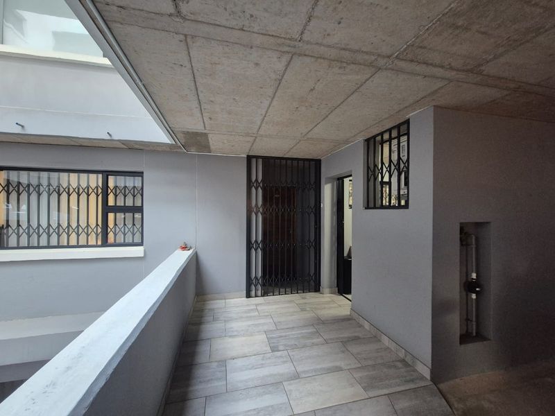 A modern, secure entrance area featuring exposed concrete ceilings, tiled flooring, and security gates, providing a clean and functional transition space.