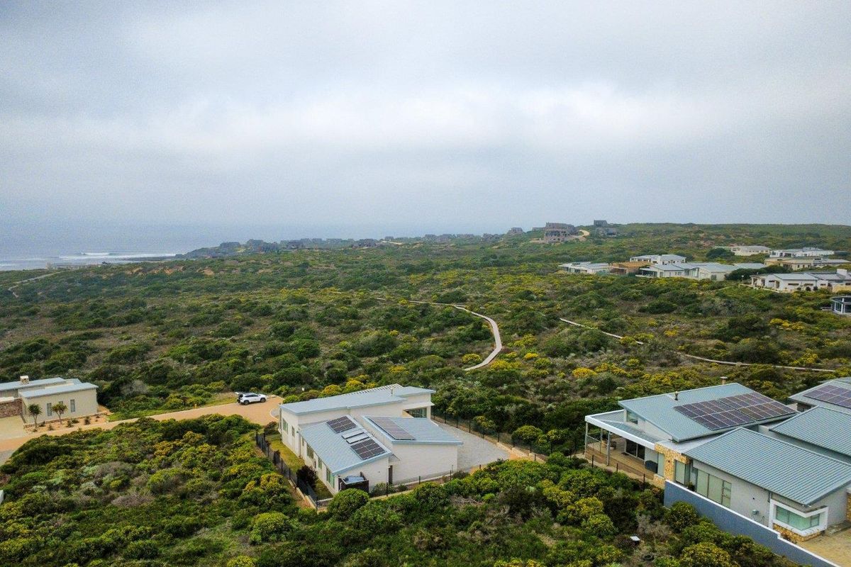Aerial view of a coastal residential property featuring modern homes with solar panels, surrounded by natural fynbos vegetation and gravel access paths.