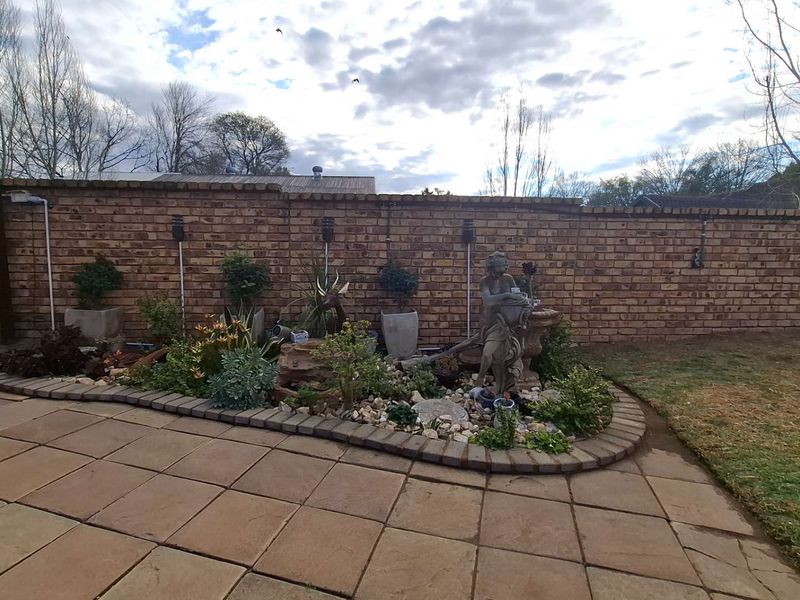 A well-maintained rear garden featuring a paved patio area, a landscaped garden bed with stone edging, and a solid brick boundary wall.