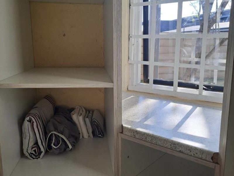 A utility storage area featuring built-in shelving, a stone-look countertop, and a window fitted with security burglar bars.