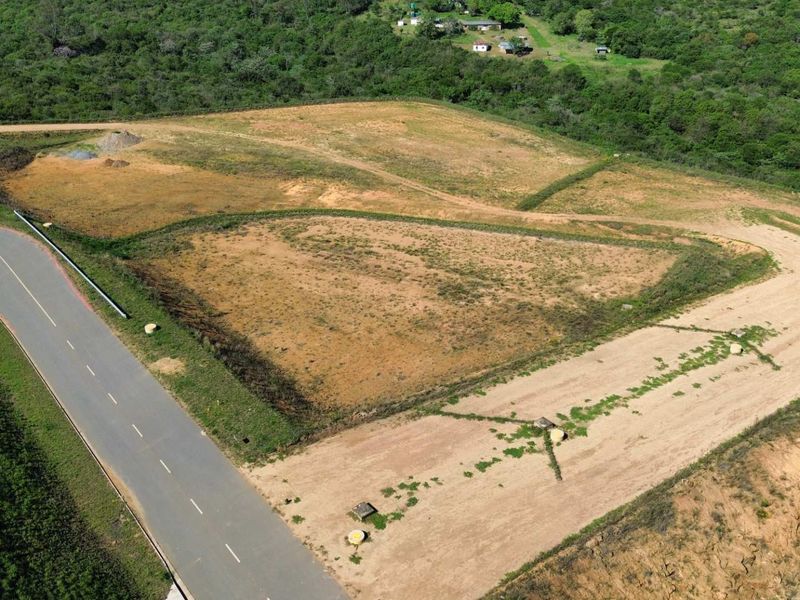 Aerial view of a large, undeveloped industrial land parcel with direct access to a paved road and surrounding natural vegetation.