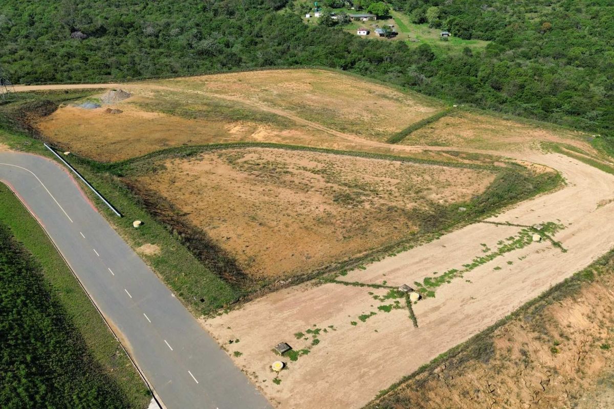 Aerial view of a large, undeveloped industrial land parcel with direct access to a paved road and surrounding natural vegetation.