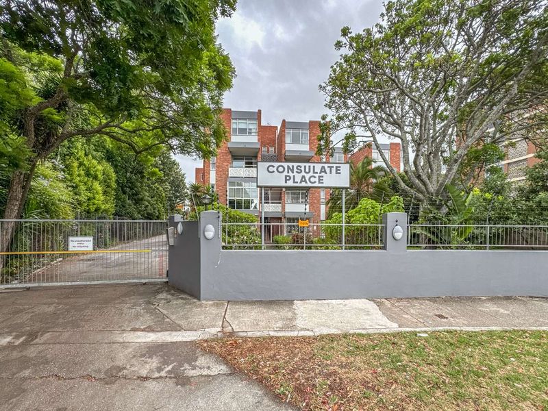 Front exterior view of Consulate Place apartment complex featuring a brick facade, secure gated entrance, and perimeter wall with electric fencing.