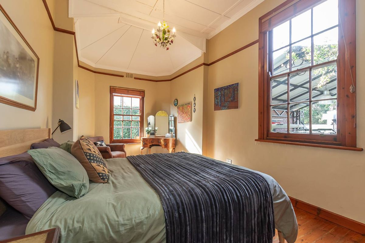 A well-lit bedroom featuring timber sash windows, polished timber flooring, and a classic coved ceiling with a central light fixture.