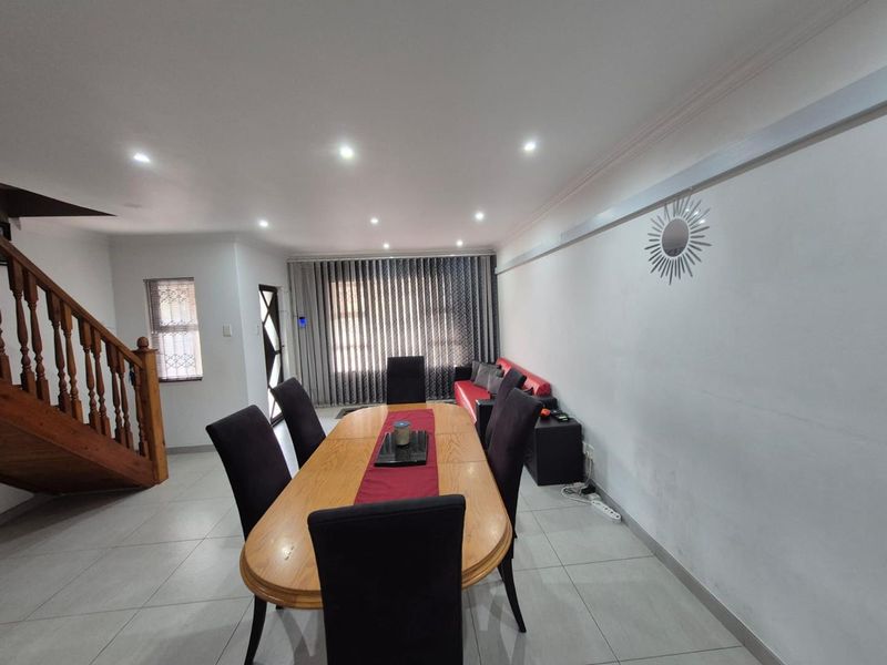 Open-plan living and dining area featuring tiled flooring, recessed downlights, and a timber staircase leading to the upper level.