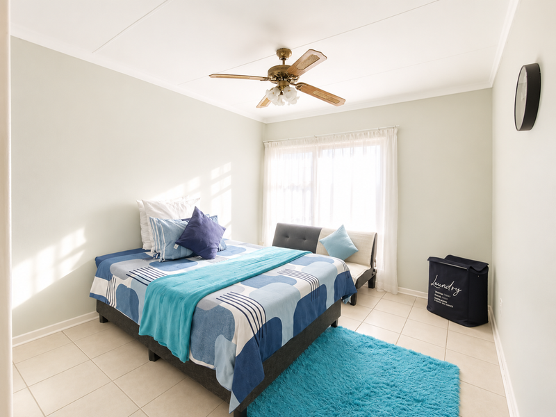 A bright bedroom featuring neutral wall tones, tiled flooring, and a ceiling fan, with natural light entering through a large sliding window.
