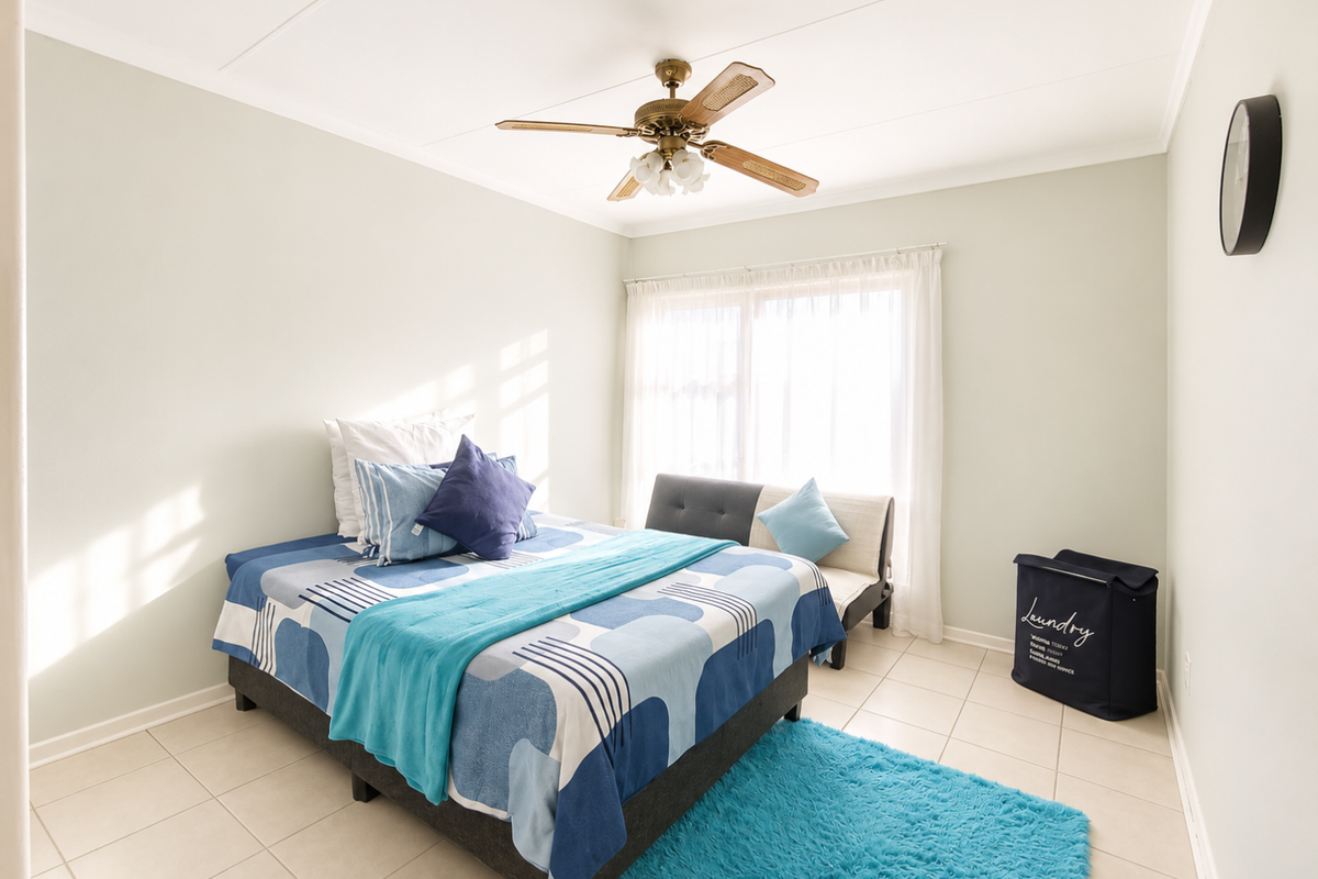 A bright bedroom featuring neutral wall tones, tiled flooring, and a ceiling fan, with natural light entering through a large sliding window.