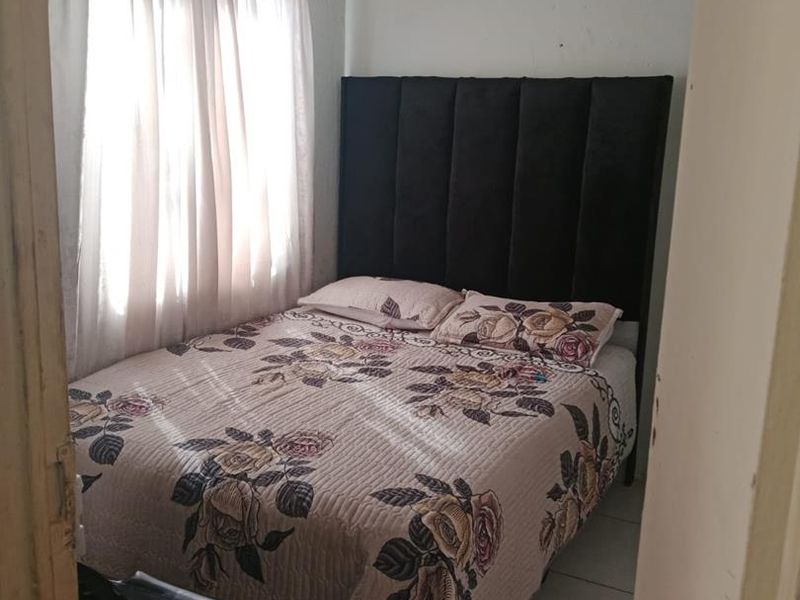 A compact bedroom featuring tiled flooring and a window with curtain rails, requiring minor cosmetic updates to the wall finishes.