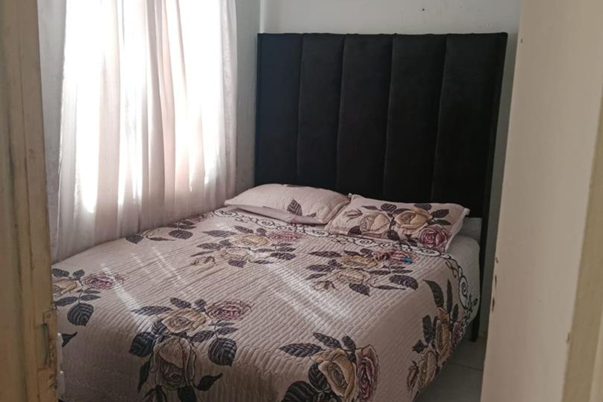A compact bedroom featuring tiled flooring and a window with curtain rails, requiring minor cosmetic updates to the wall finishes.