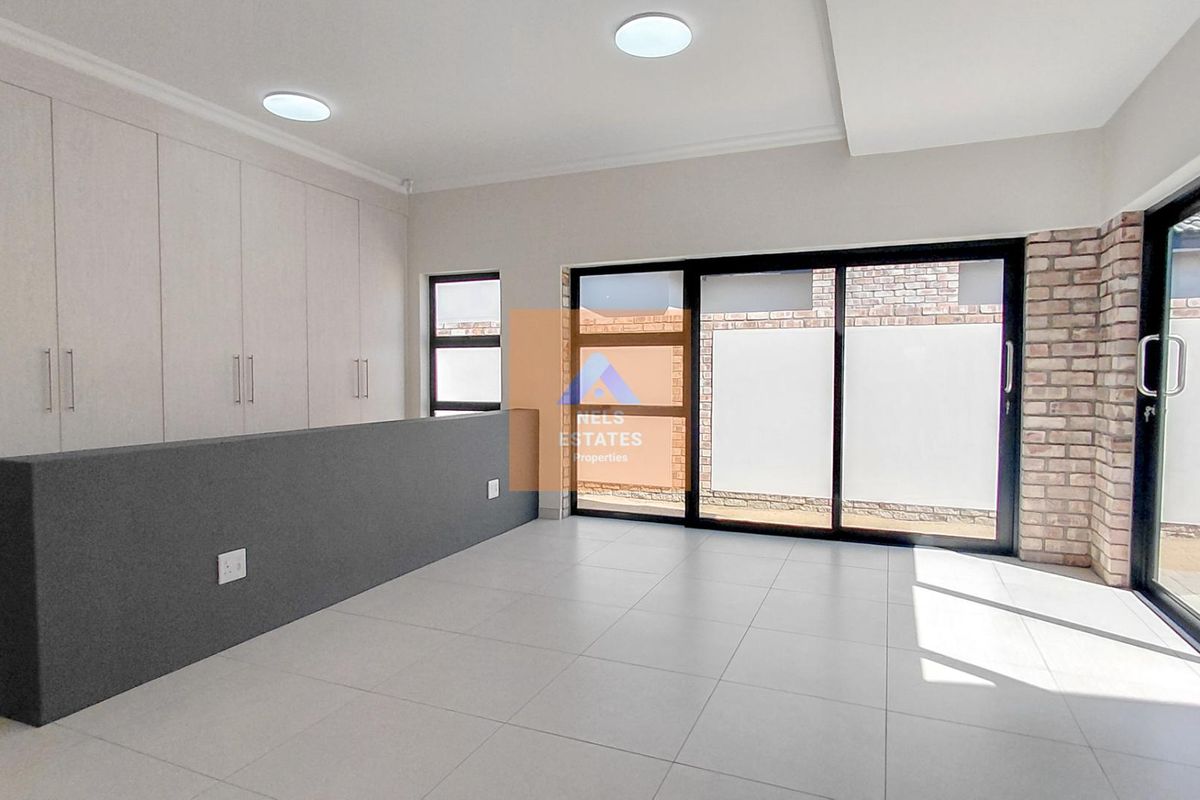 A bright, modern living area featuring neutral tiled floors, extensive built-in cabinetry, exposed brick accents, and large sliding glass doors leading to the exterior.