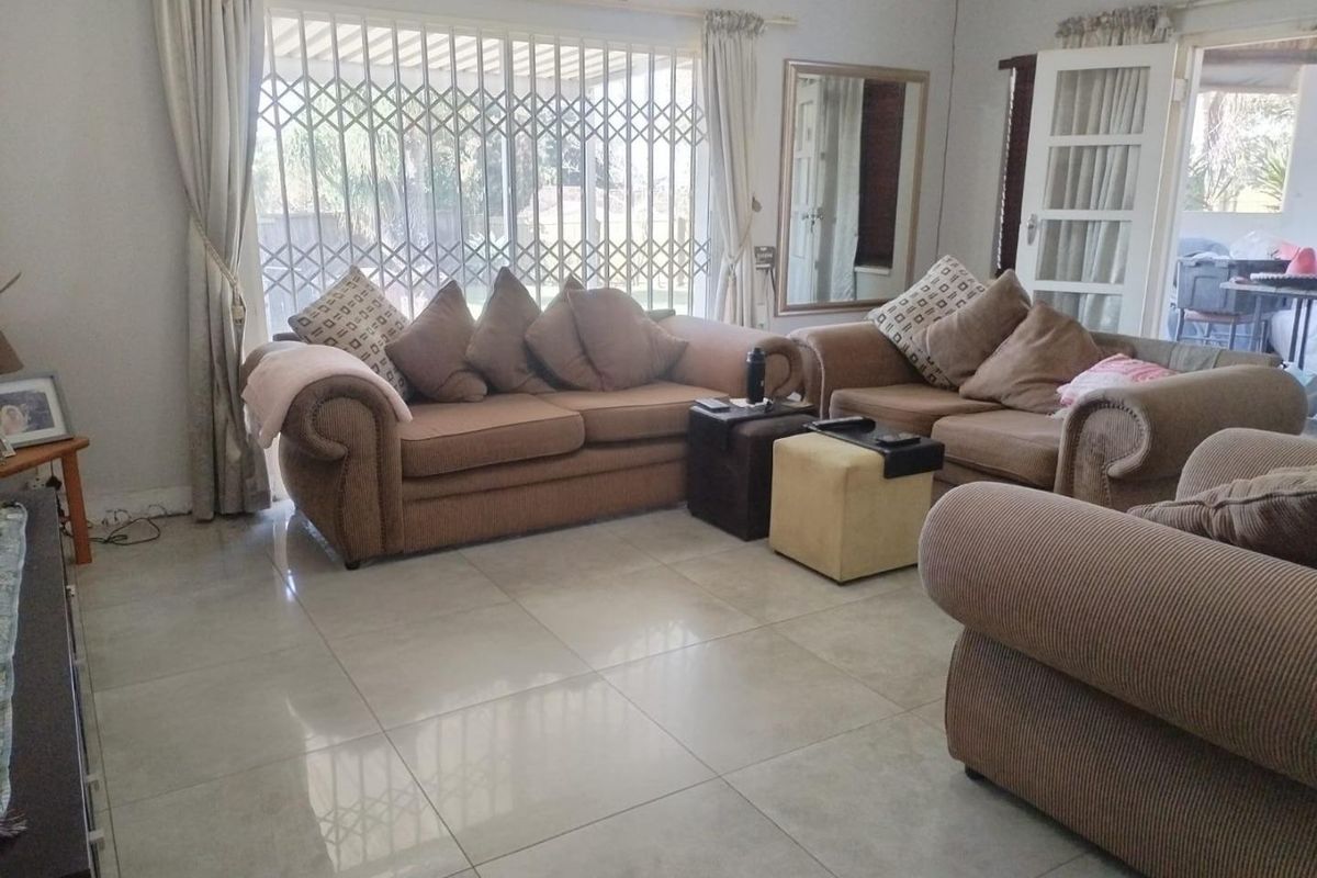 A spacious living room featuring large format floor tiles, a security gate, and a sliding door providing access to the outdoor area.