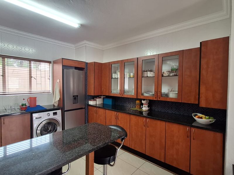 A functional kitchen featuring wood-finish cabinetry, granite countertops, glass-fronted display units, and integrated laundry facilities.