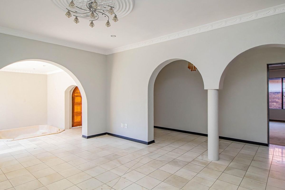 Spacious open-plan living area featuring distinctive arched doorways, decorative ceiling detailing, and neutral tiled flooring throughout.
