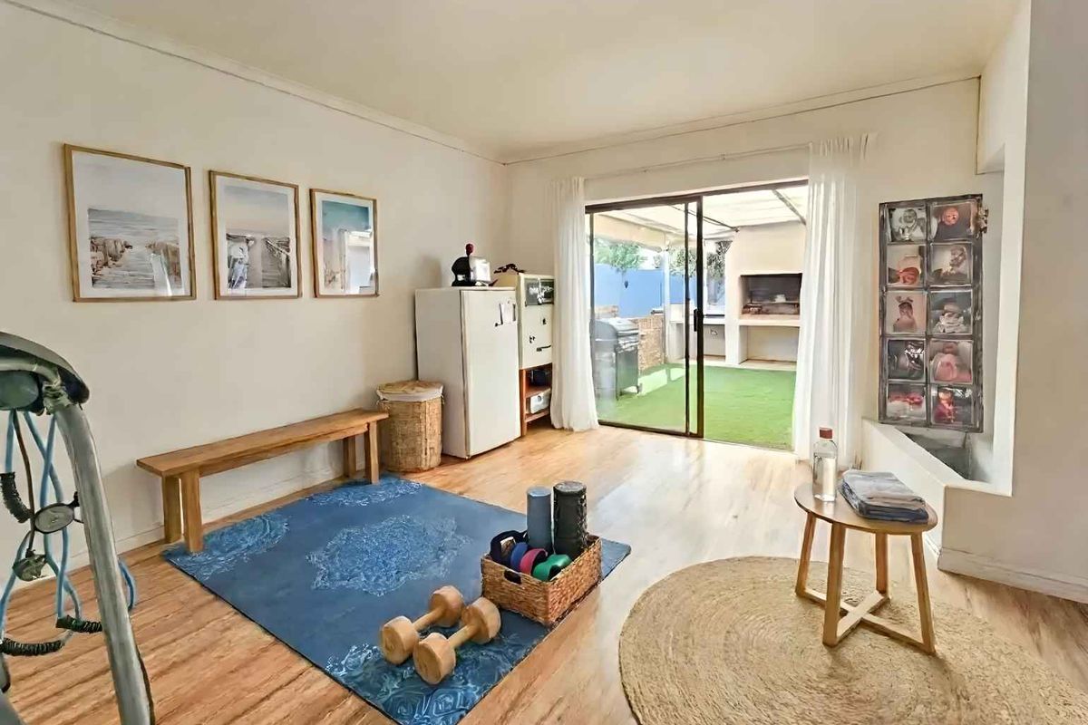 A multi-purpose living space featuring wood-look flooring and sliding glass doors that open onto a covered patio with a built-in braai area.
