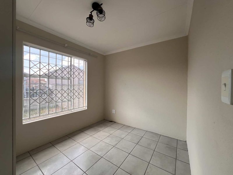 A vacant bedroom featuring neutral tiled flooring, a window with security bars, and a central ceiling light fixture.