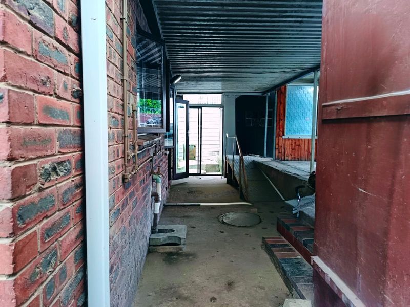 A covered outdoor patio area featuring brick walls, concrete flooring, and a corrugated metal roof, providing a functional transition space between the home and garden.