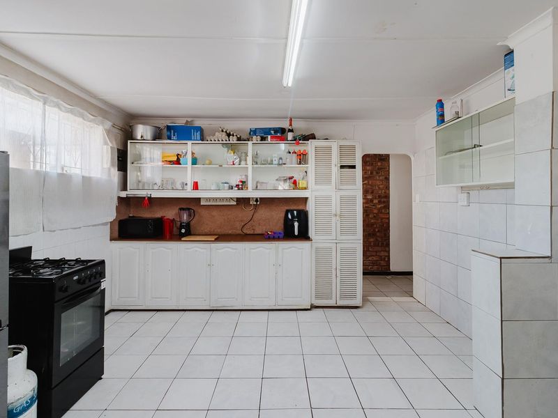 A functional kitchen featuring white cabinetry, tiled splashbacks, tiled flooring, and a gas stove, offering a practical layout with potential for modern updates.