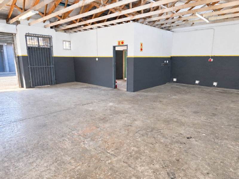 Spacious industrial garage featuring exposed timber roof trusses, concrete flooring, a secure roller shutter door, and a dedicated internal access point.