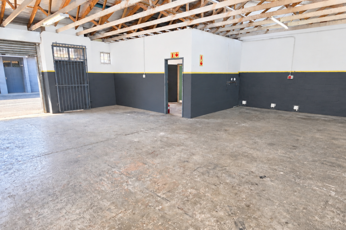 Spacious industrial garage featuring exposed timber roof trusses, concrete flooring, a secure roller shutter door, and a dedicated internal access point.