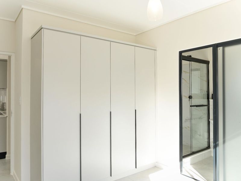 A bright, modern bedroom featuring a large built-in wardrobe and an en-suite shower with a sleek black frame.