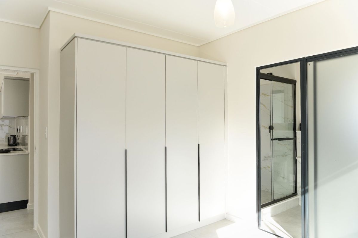 A bright, modern bedroom featuring a large built-in wardrobe and an en-suite shower with a sleek black frame.