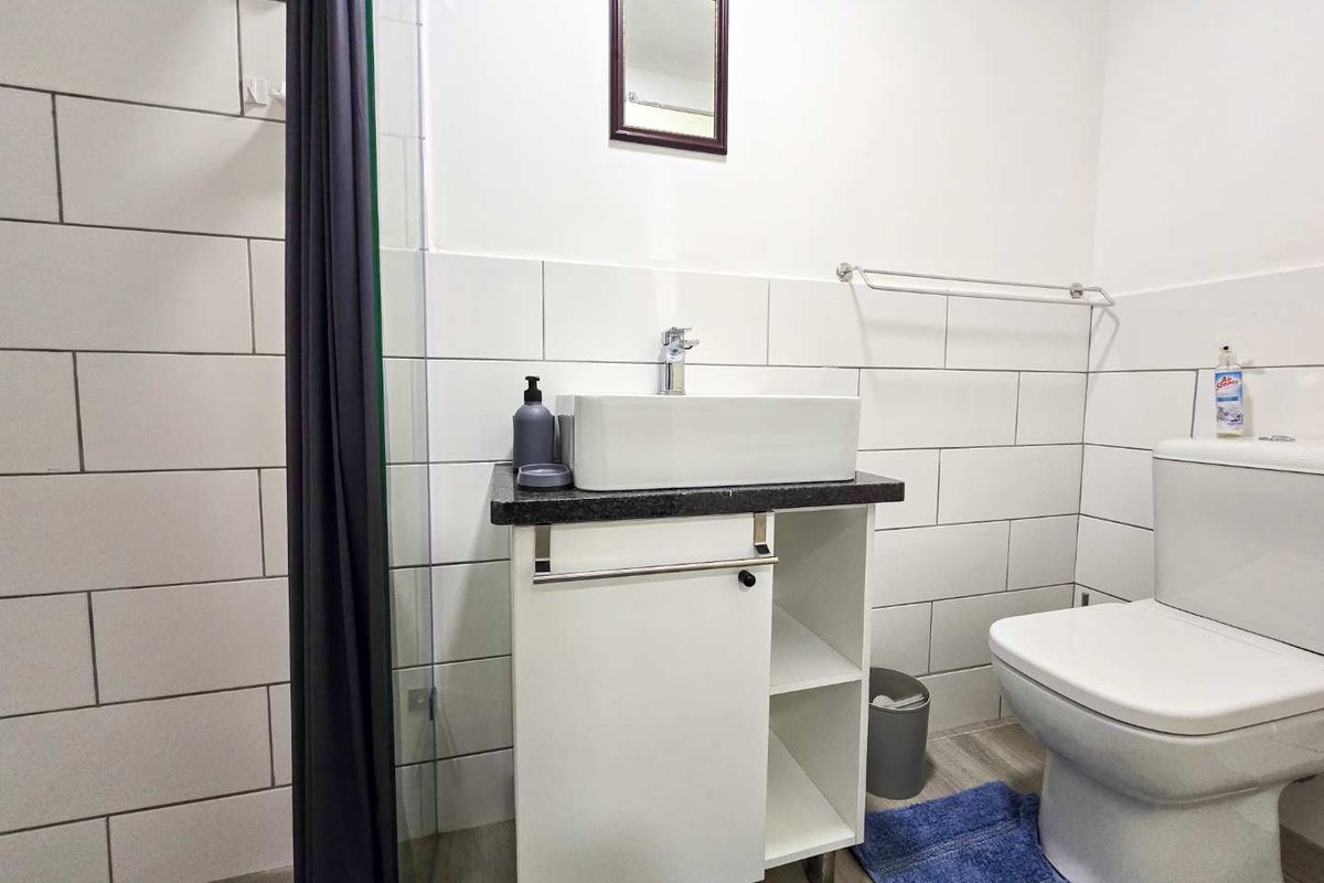 A functional bathroom featuring a modern vessel sink vanity, a walk-in shower with glass enclosure, and a standard toilet with white wall tiling.