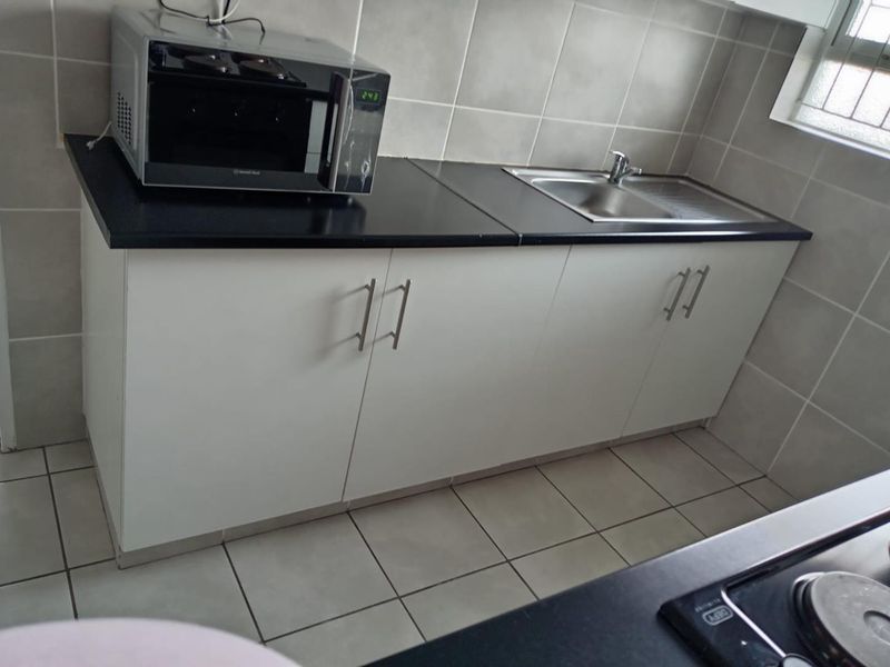 A functional kitchen area featuring white cabinetry, dark laminate countertops, a stainless steel sink, and neutral ceramic tiling throughout.