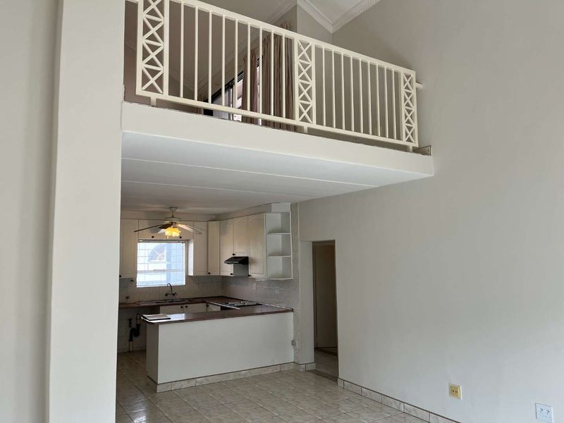 Open plan living area featuring a mezzanine level with metal balustrade and a functional kitchen with built-in cabinetry and appliances.