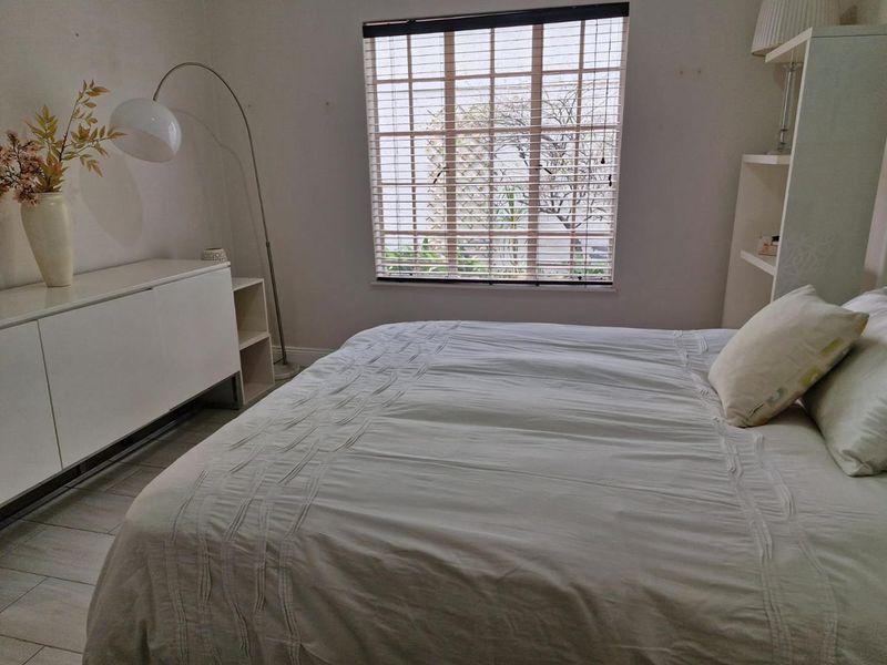 A bright bedroom featuring tiled flooring, built-in shelving, and venetian blinds, offering a neutral canvas for personalization.