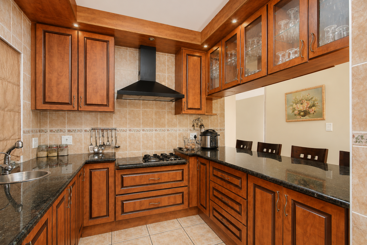 A well-maintained kitchen featuring warm-toned wooden cabinetry, granite countertops, a gas hob with an extractor fan, and integrated glass-fronted display cabinets.