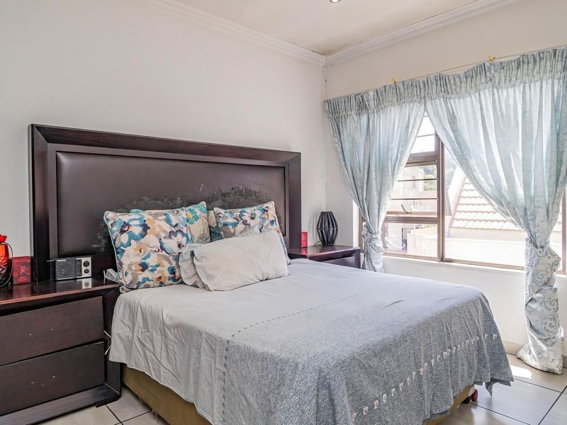 A standard bedroom featuring tiled flooring, neutral walls, and a large window with natural light, providing a functional and comfortable living space.