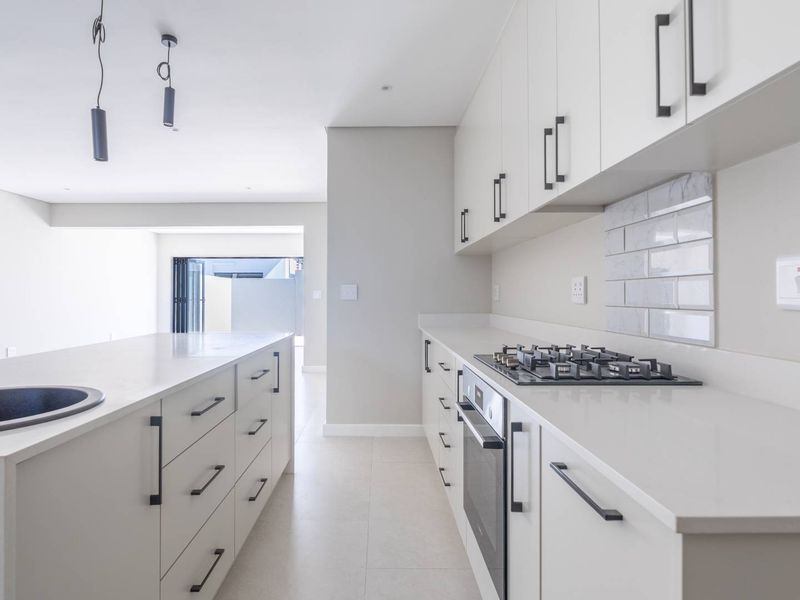 Modern kitchen featuring sleek white cabinetry, stone countertops, a gas hob, built-in oven, and stylish subway tile backsplash in a bright, open-plan layout.