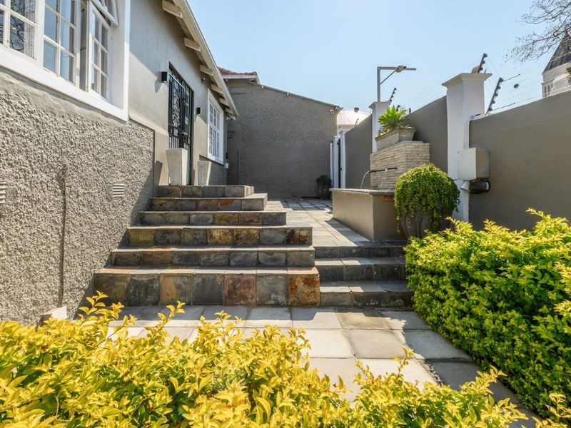A well-maintained rear courtyard featuring stone steps, paved patio area, and a built-in water feature enclosed by a secure boundary wall.