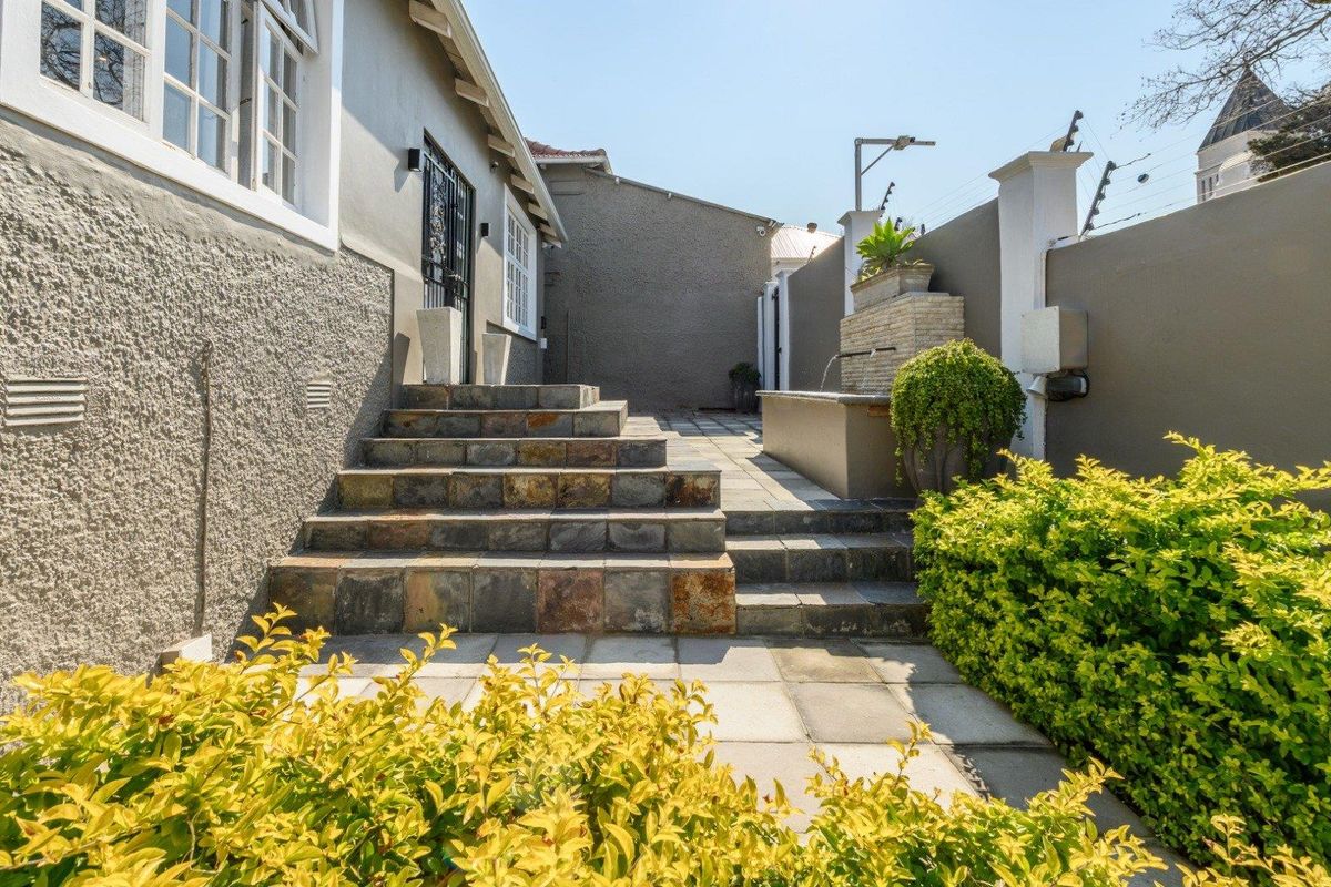 A well-maintained rear courtyard featuring stone steps, paved patio area, and a built-in water feature enclosed by a secure boundary wall.