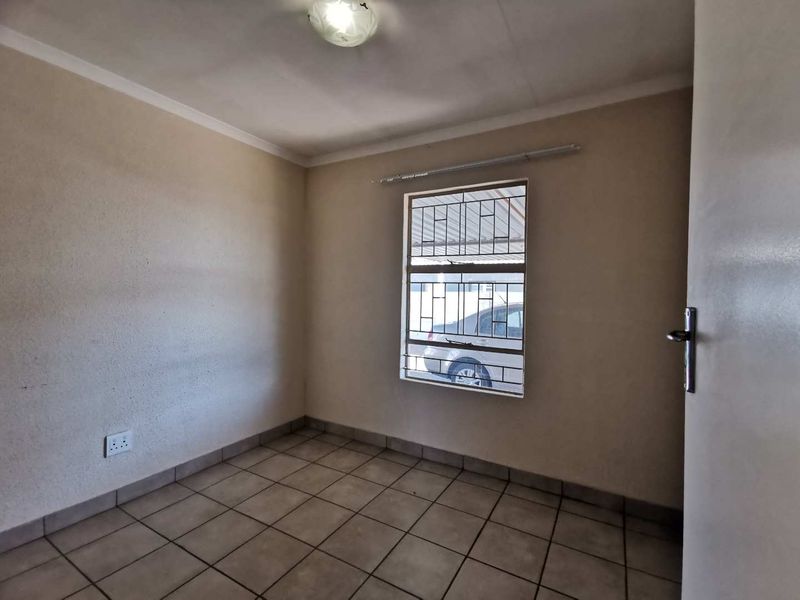 A clean, empty bedroom featuring tiled flooring, a window with security bars, and neutral wall finishes, ready for personalization.