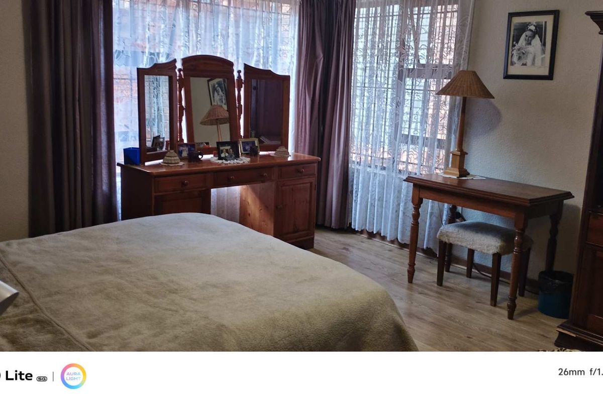 A bedroom featuring wood-look flooring and large windows with curtains, providing a functional and comfortable living space.