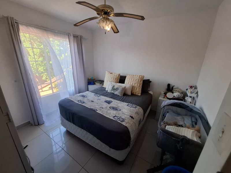 A functional bedroom featuring tiled flooring, a ceiling fan, and a built-in cupboard, with natural light provided by a large window.