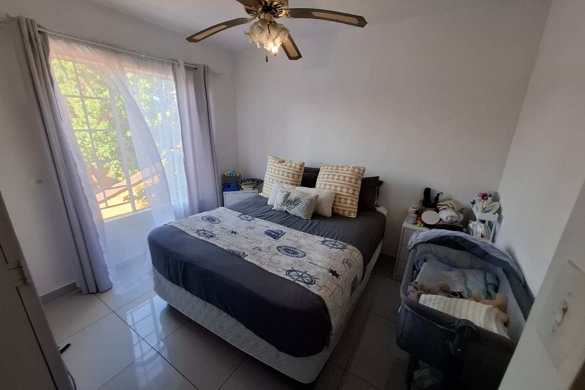 A functional bedroom featuring tiled flooring, a ceiling fan, and a built-in cupboard, with natural light provided by a large window.